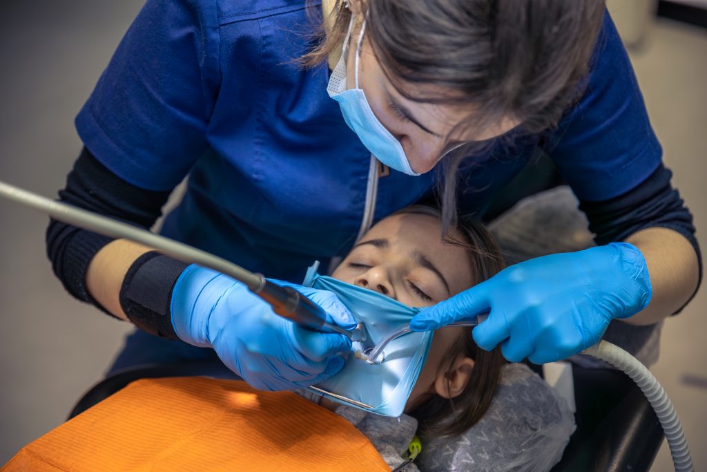 The dentist treats the child’s tooth using a rubber dam. Close-up of tooth treatment.